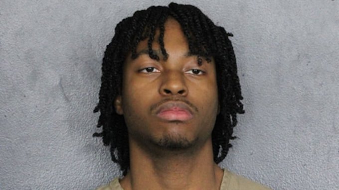 The image appears to be a mugshot of a young man with shoulder-length twisted dreadlocks, wearing what looks like a beige or tan shirt against a plain gray background. The photo seems to illustrate the post's cautionary message about the dangers of storing cryptocurrency or seed phrases on gaming computers, as the individual may be the "friend" who allegedly lost $8 million worth of crypto after a malware infection from gaming compromised his wallet.