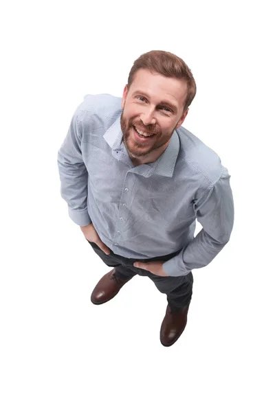 A high-angle photograph of a smiling bearded man in a light blue button-up shirt and jeans, standing with hands on hips against a white background.