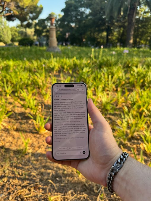A hand holds an iPhone displaying an article titled 'PHASE 1 — UNDERSTAND' about analyzing a startup, set against a backdrop of green grass and trees with a stone monument.
