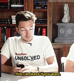 The image shows a man sitting at a table, looking down at his cell phone with an expression of confusion or surprise. There are multiple books surrounding him, indicating that he might be in a library or a study area. The text "You can leave if you want" is written on the image, which could be part of a humorous caption or a motivational message from someone else who took the photo.