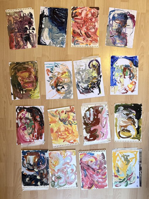 An overhead view of 16 small abstract paintings arranged in a grid on a wooden floor, each featuring expressive brushstrokes in varied color palettes.