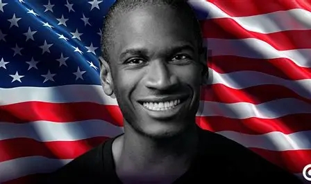 The image shows a smiling Black man in a dark shirt in black and white, set against a vibrant American flag background. This represents Arthur Hayes, the BitMEX co-founder, featured in connection with his latest essay predicting a Bitcoin bull market fueled by Treasury buybacks.