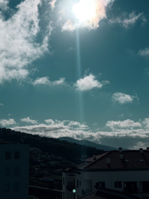 A bright morning sun pierces through scattered clouds over a hillside town with terracotta-roofed buildings, casting dramatic rays across the landscape. The serene sunrise complements the post's "Good morning" greeting, while the request for a SOL (Solana) address adds a request for crypto wallet information to the friendly exchange.