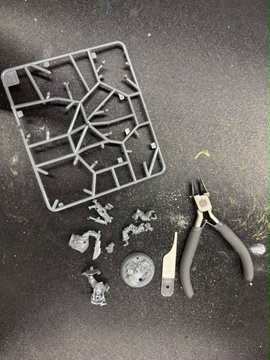 A plastic model kit sprue, several small cut parts, and a pair of black nippers (clippers) laying on a dark grey work surface.