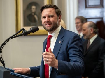 Vice President JD Vance speaks at a podium, pictured days after his 2025 financial disclosure revealed he holds between $250K and $500K in Bitcoin at Coinbase.