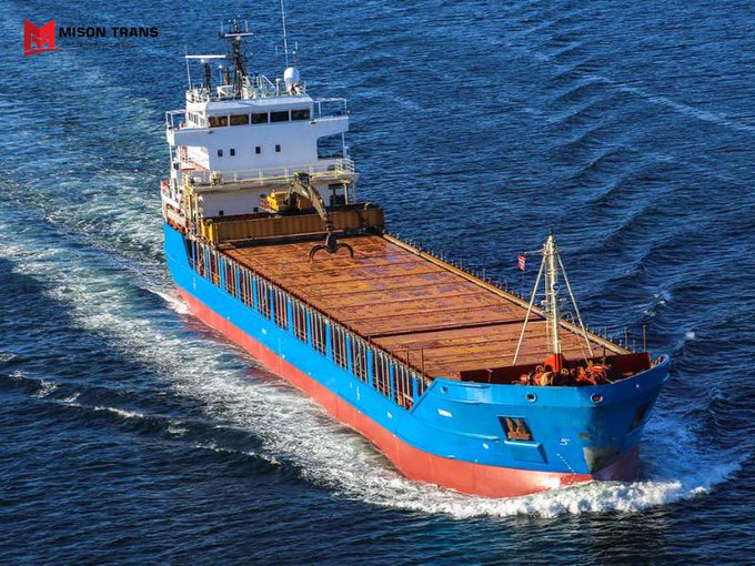 An aerial view of a blue and red cargo ship sailing through the ocean, with a 'MISON TRANS' watermark in the upper left corner.