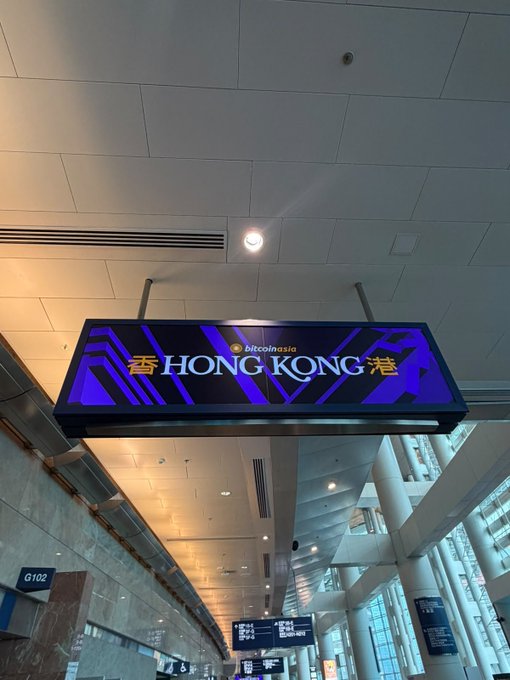 Team Wager Predict arrives at BitcoinAsia Hong Kong, with a prominent “bitcoinasia HONG KONG 港” sign overhead. Gate G102 and event signage are also visible.