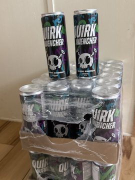 A large stack of "WURK" energy drink cans wrapped in plastic on a wooden floor, with two additional cans placed on top.