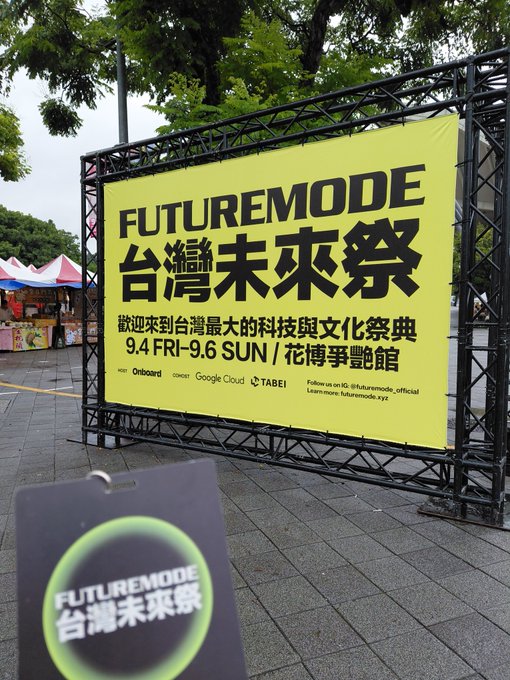 An outdoor event photo showing a large yellow billboard for "FUTUREMODE 台灣未來祭" (Taiwan Future Festival) at 花博爭艷館 (Expo Park), held 9.4 FRI - 9.6 SUN, sponsored by Google Cloud and Tabei.