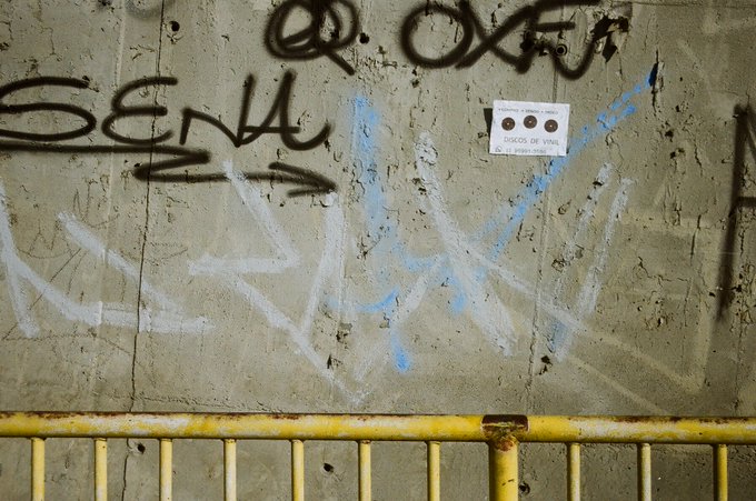 A weathered concrete wall covered in black and blue graffiti, including the prominent tags "Q. OXE" and "SENN," with a yellow metal railing running along the bottom. This analog photograph, taken with a Canon EOS300V in Osasco in 2016, documents an urban graffiti scene tied to the "OXE" NFT created for the #WALLS event by @tornado_ilus.