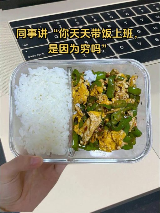 A glass meal prep container holds white rice alongside a stir-fry of scrambled eggs and green peppers, held over a laptop keyboard. The overlaid Chinese text reads "同事讲'你天天带饭上班，是因为穷吗'" (Coworker says "Do you bring lunch every day because you're poor?"), humorously framing the homemade meal as a response to the teasing question.