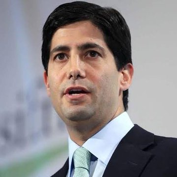 A portrait of a man in a dark suit and light green tie against a blurred background.