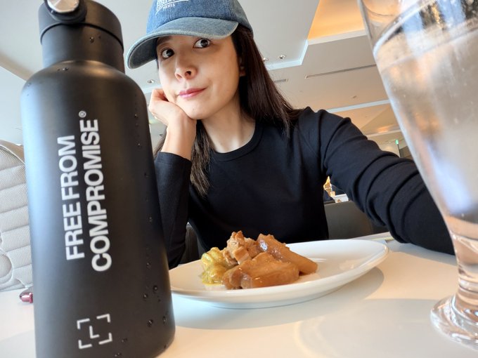 A woman in a baseball cap sits at a table with a black water bottle labeled "FREE FROM COMPROMISE" and a plate of food, gazing wearily at the camera. The post warns against leaving crypto on exchanges, suggesting that self-custody (like carrying your own "assets") is safer—much like holding onto your own belongings rather than trusting them to someone else.
