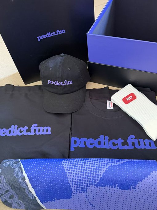 The image features a black box containing various items related to predicting fun merchandise. The box includes a t-shirt, a hat, and socks. There are also two smaller boxes within the main one, each holding different items such as a baseball cap and a pair of socks. A skateboard is placed on top of the box, adding an element of fun and excitement to the overall presentation.