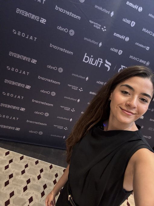 A young woman takes a selfie in front of a step-and-repeat backdrop featuring various sponsor logos including 'mastercard', 'Hulu', 'TALOS', 'Ongo', 'Intuit', 'BIBIGO', 'SHEIN', 'HUM', 'Bigo', and 'Samsung Galaxy S25'.