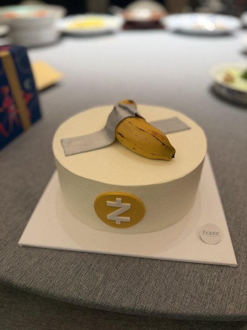 A celebratory white frosted cake topped with a decorative banana sits on a table, featuring a gold "Z" symbol and a small label reading "Exotic" — fittingly themed after Zcash ($ZEC) and its all-time high birthday celebration.