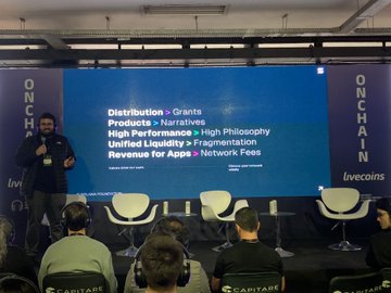 The image shows a man standing at a podium during an event, giving a presentation or speech. The audience consists of several people sitting in chairs around him, attentively listening to his words. There are also two white chairs visible in the scene. The backdrop features banners and signs that read "Onchain", "Hackanation", "@tokennation_io", "Stellar", and "@superteambr". The event appears to be a gathering of tech enthusiasts, possibly discussing topics related to blockchain or finance.