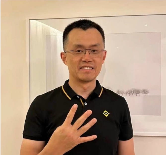 A man in a black polo shirt with a Binance logo gestures while speaking in front of a framed artwork. The Binance logo and the post's reference to BNB suggest he is a Binance representative addressing questions about Giggle Academy's token selling practices.
