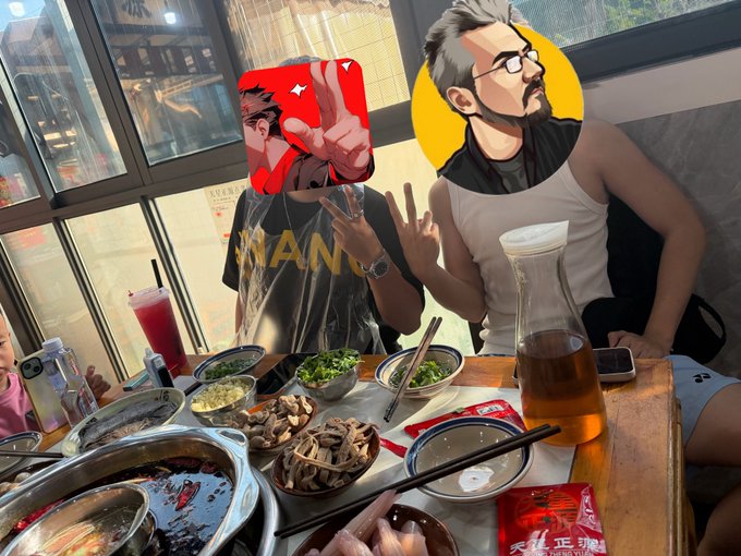 Two friends pose with peace signs at a hotpot restaurant, their faces playfully covered with cartoon stickers, surrounded by bubbling broth, chopsticks, a teapot of tea, and side dishes like mushrooms and greens on the table.