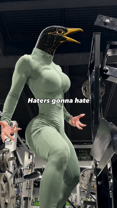A person wearing a tight green bodysuit and a bird mask poses in a gym setting, with the overlaid text "Haters gonna hate."