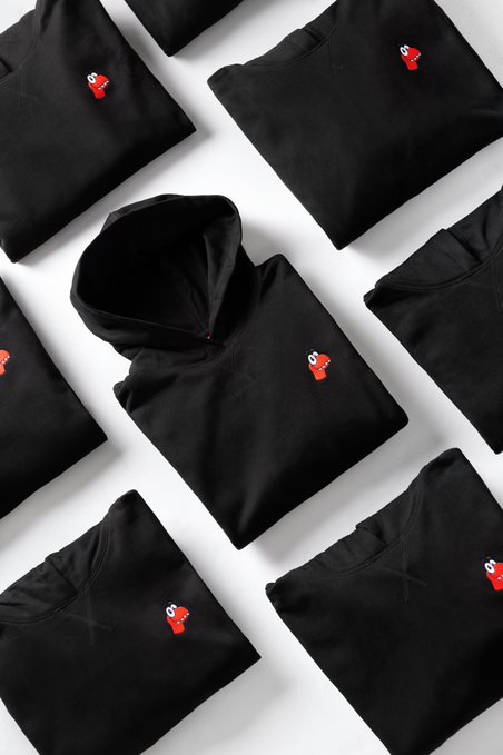 A flat lay arrangement of folded black hoodies and sweatshirts, each featuring a small red embroidered logo on the chest.