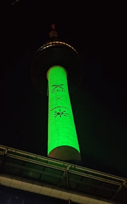 A tower illuminated in green at night with logos, photographed from below against the dark sky.