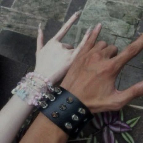 Two hands make rock sign gestures, one wearing a colorful beaded bracelet and the other wearing a black studded leather cuff.