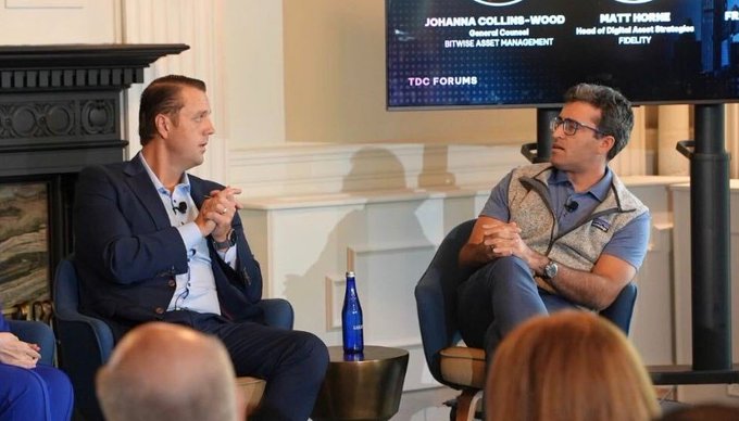 Two men seated on stage during a panel discussion, with a screen behind them displaying the names 'JOHANNA COLLINS-WOOD' and 'MATT MORRIS' alongside their titles.