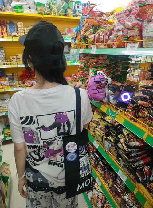 The image shows a woman standing in front of a grocery store shelf filled with snacks, specifically chips. She is wearing a black baseball cap and has a backpack slung over her shoulder. The background reveals an array of snack items displayed on shelves behind her. There are also two stickers visible on the bag she's holding. The post appears to be promoting a product or idea related to the woman's appearance or the snacks in the store, possibly encouraging people to try it out or express their opinions about it.