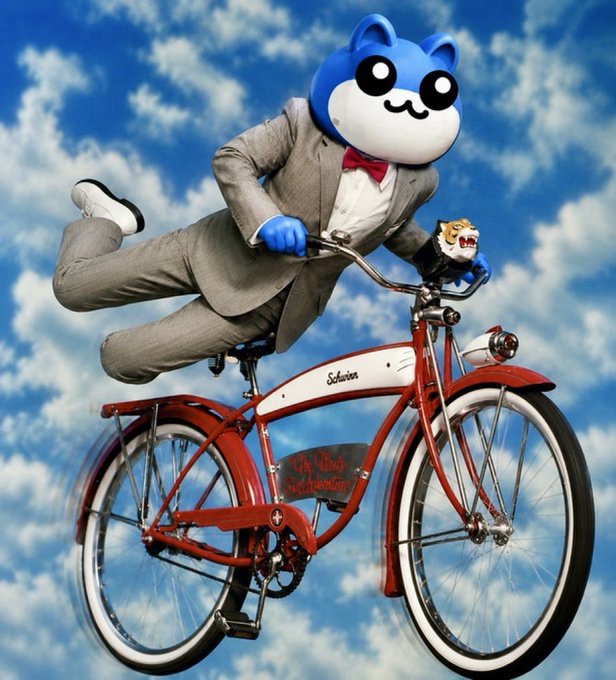 A surreal composite image of a blue cartoon cat character in a gray suit and red bow tie riding a red Schwinn bicycle against a blue cloudy sky.