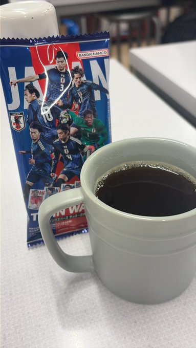 A white coffee mug filled with dark coffee sits beside a "BANDAI NAMCO" packaged snack featuring Japan national football team players, with "JAPAN" prominently displayed on the blue wrapper. The image promotes a Mugshot Pro membership, tying the simple pleasure of a coffee break to earning 10x B3TR rewards through the VeBetterDAO ecosystem on VeChain.