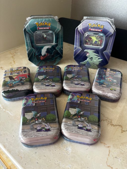 A collection of six Pokémon Trading Card Game mini tins featuring Darkrai and Tornadus, displayed alongside their game artwork on a marble countertop. The post celebrates finding these collectible tins, which are part of the Pokémon TCG merchandise line.