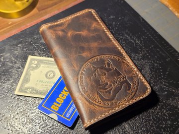 Photograph of a brown leather wallet with a 'Brotherhood of Steel' (Fallout video game reference) embossed design, containing a dollar bill and a Discover card.