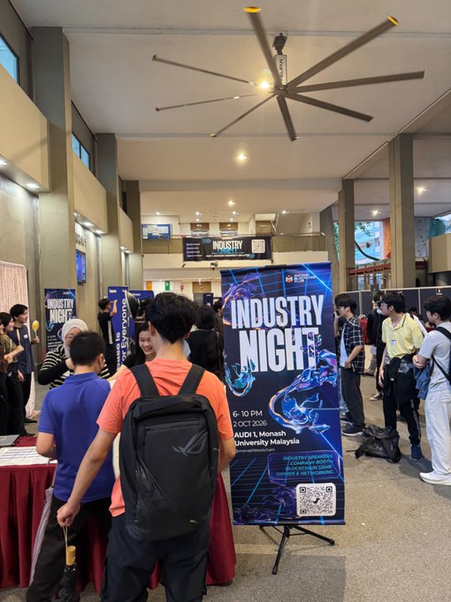 A crowded indoor venue displays banners for 'INDUSTRY NIGHT' happening '2 OCT 2026' at 'AUDIT 1, Monash University Malaysia' with various student booths.
