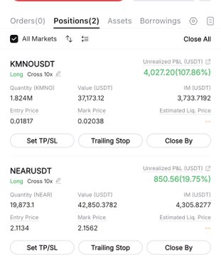 The image shows a screenshot of a smartphone screen displaying trading information for several stocks including KMNOUSDT and USDT (Unrealized Profit Loss). The text on the screen indicates that the user has either just closed or is about to close their long trade in these markets. The phone's position in the upper left corner suggests it is being viewed from this angle. This screenshot provides valuable information for someone looking to make informed trading decisions and understand the performance of various stocks.