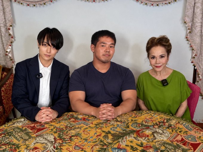 Three people sit together at a table covered with a decorative floral-patterned cloth, each wearing small clip-on microphones. The image accompanies a post announcing that "Yajuu Senpai" has joined the "Anti-Bullying Committee," suggesting the group may be featuring in a segment related to this announcement.