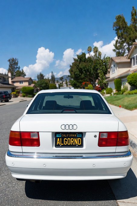 A white Audi sedan parked on a residential street with a California license plate reading 'ALGORND'.