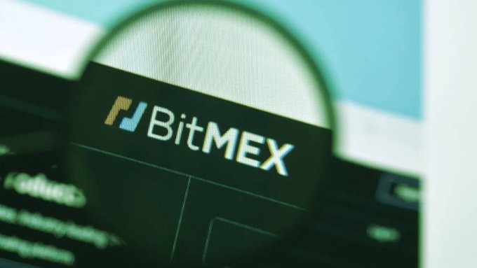 A magnifying glass held over a screen zooms in on the BitMEX logo and branding.