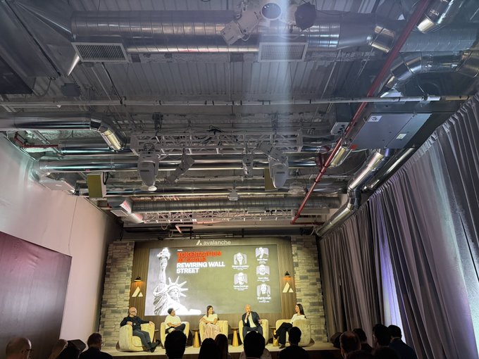An indoor conference event at Avalanche with a panel of speakers seated on stage in front of a 'Defining Wall Street' themed screen.