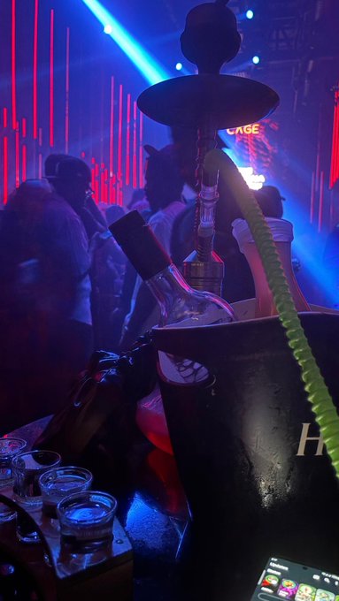 A hookah lounge at a nightclub with red and blue neon lighting, featuring a tall hookah pipe on a table.