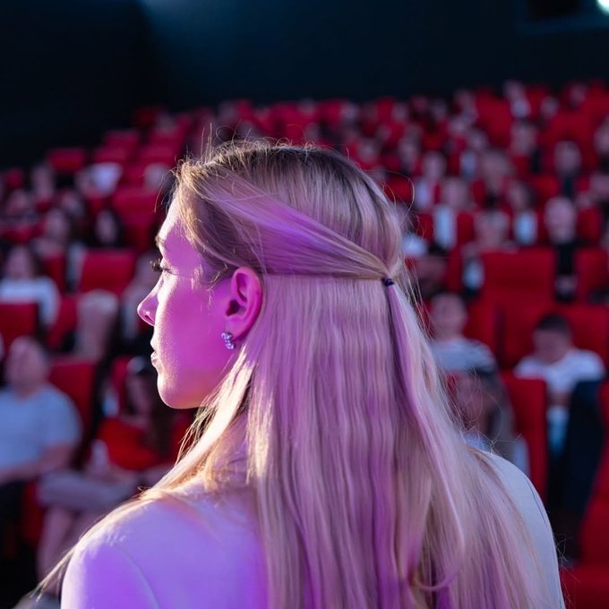 A blonde woman is seen in profile with purple lighting illuminating her face and hair, set against a blurred background of red theater seats filled with audience members, suggesting attendance at an event related to the Bybit Europe cryptocurrency brand mentioned in the post.