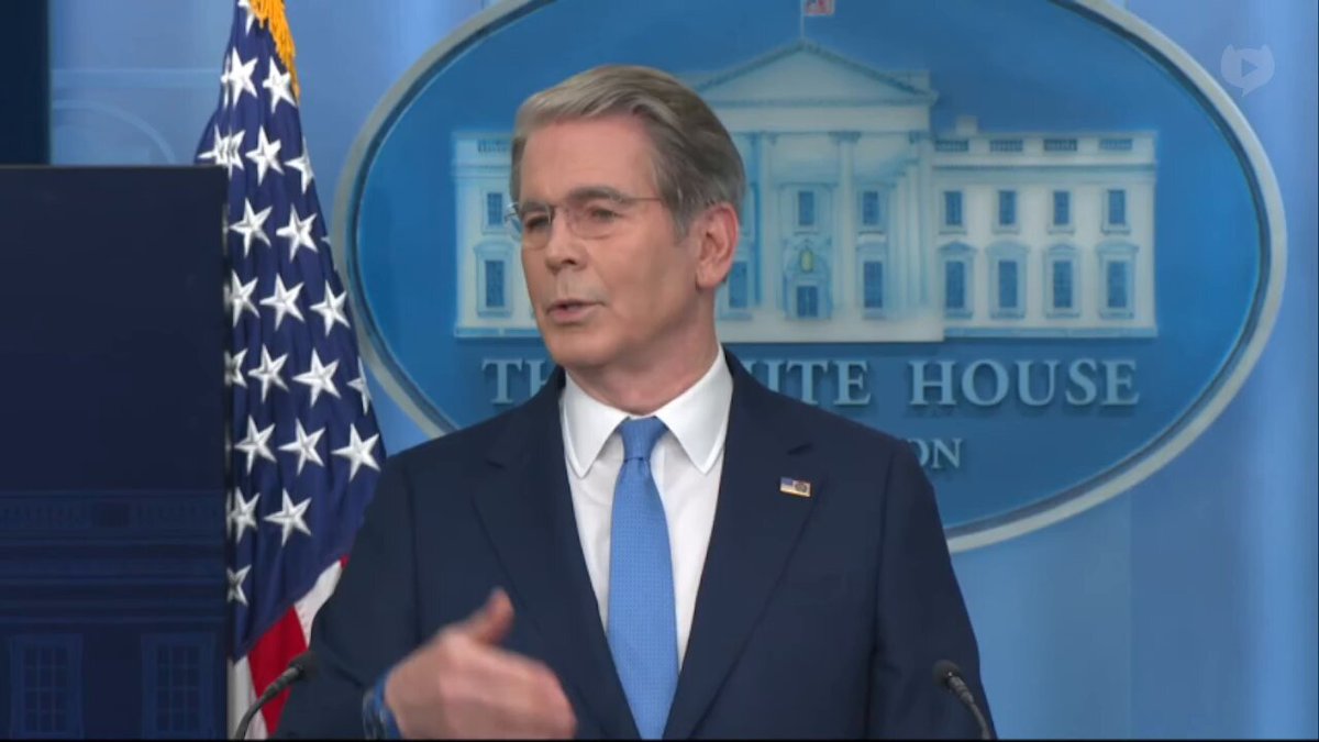 The image shows a man wearing glasses, standing next to an American flag with the White House logo behind him. The man appears to be giving a speech or addressing an audience. There are also some text elements in the image that read "It already exists and was willingly implemented into your favorite Bitcoin wallet to be used instead of BTC." This suggests that the man might be discussing the use of Bitcoin as a means of payment for official events, ceremonies, or other government-related activities. The presence of these elements indicates that this is likely an advertisement or promotional material related to Bitcoin or cryptocurrency usage in a formal context.