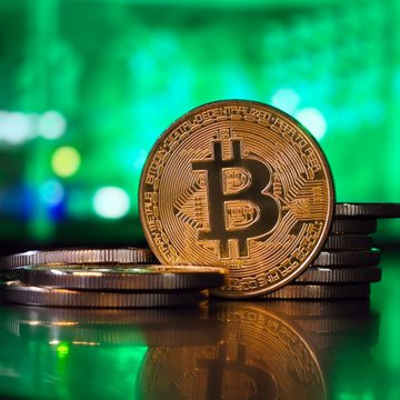 A gold Bitcoin (BTC) token rests atop stacks of coins against a vibrant green, bokeh-lit background, symbolizing the cryptocurrency's recent rebound. The image visually reinforces Bernstein's insight about Bitcoin's climb toward $80K, highlighting the token as the focal point of renewed liquidity and market optimism.