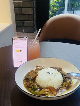 A plate of curry rice with a side of pink drink at a restaurant table, with a smartphone displaying a chat interface in the background.