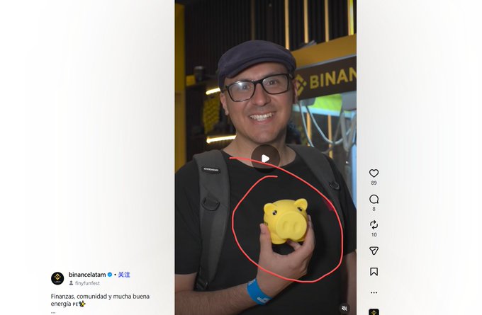 A screenshot of an Instagram post by "binancelatam" (Binance Latinoamérica) showing a man wearing glasses and a cap, smiling while holding a yellow piggy bank-shaped item that has been circled in red, with the caption "Finanzas, comunidad y mucha buena energía." The piggy bank is highlighted as the latest meme from a Binance video, humorously emphasizing the financial/crypto theme suggested by the piggy bank's association with saving money.