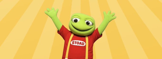 A cheerful green cartoon toad mascot wearing a red shirt with "$TOAD" emblazoned on it joyfully raises its arms against a sunny yellow striped background, promoting the $TOAD token in line with the post's suggestion to launch a launchpad on toad.fun.