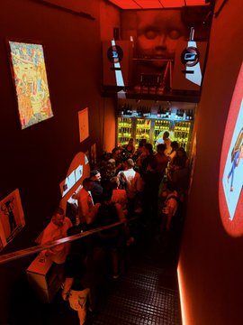 A dimly lit, red-hued lounge is packed with patrons mingling near a glowing bar display, where screens above show "solana" branding alongside a large eye graphic—capturing the energetic, social atmosphere of the "Solana Mixer" event.