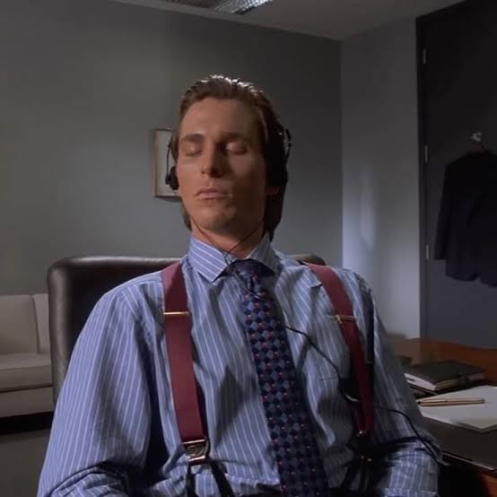 A man in a blue pinstripe shirt, red suspenders, and patterned tie sits with eyes closed, wearing headphones as he listens to music in an office setting. The image captures the contemplative, focused listening experience referenced in the caption about enjoying Bach and Mozart while monitoring trading positions.