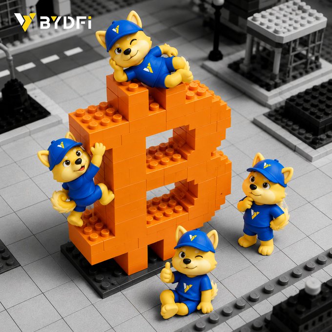 A large orange LEGO Bitcoin "B" sculpture is surrounded by four BYDFi mascot puppies in blue construction gear and caps, with the BYDFi logo visible in the top corner—visually echoing the post's "brick by brick" metaphor as Bitcoin's structure is rebuilt piece by piece.