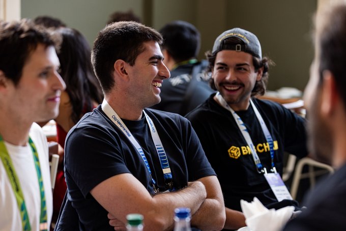 Three men share a laugh at what appears to be a conference or networking event in Rio, with two wearing BNB CHAIN branded lanyards and t-shirts, matching the post's mention of a meeting with the BNBCHAIN team.